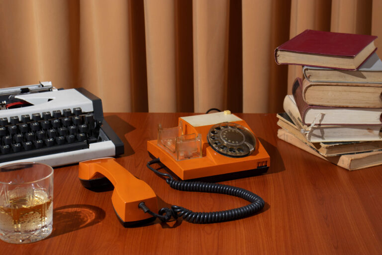 Escriptori amb màquina d’escriure, telèfon antic i llibres desordenats, simbolitzant sistemes obsolets i falta d’automatització.